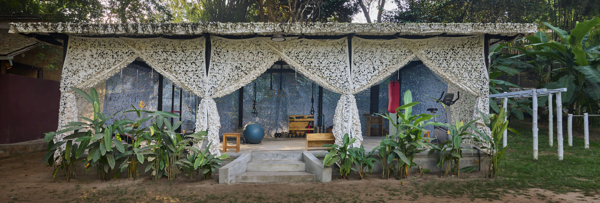 A luang prabang in the middle of a grassy area, adorned with curtains and plants.