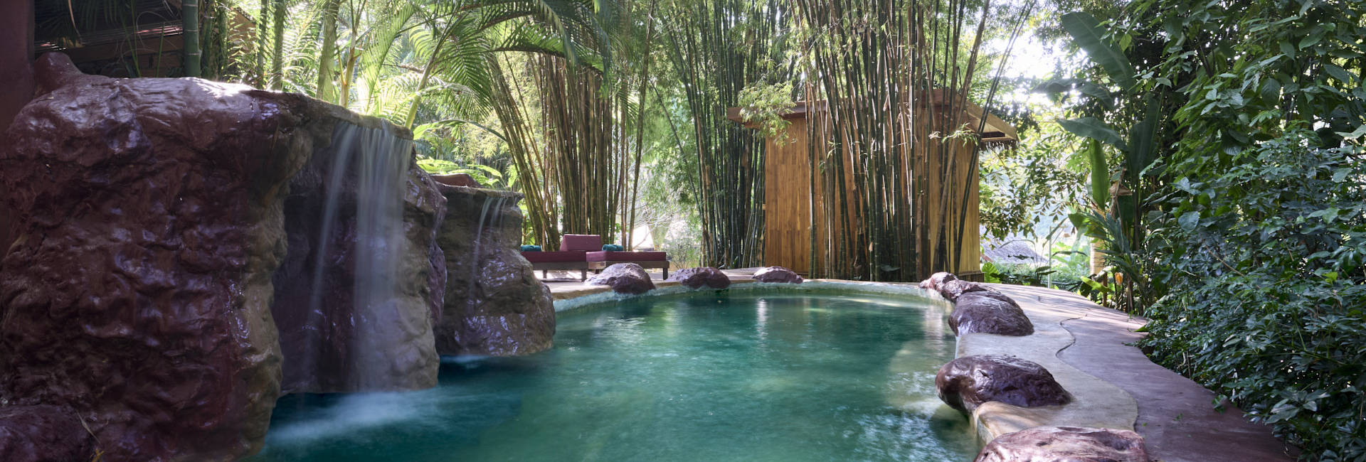 In the beautiful town of Luang Prabang, a pool nestled amidst lush trees is enhanced by a mesmerizing waterfall.