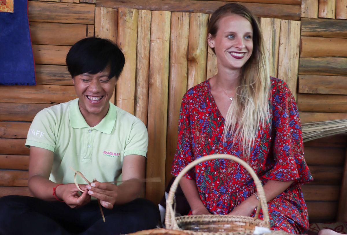 A woman and a man smiling while engaging in bamboo weaving.