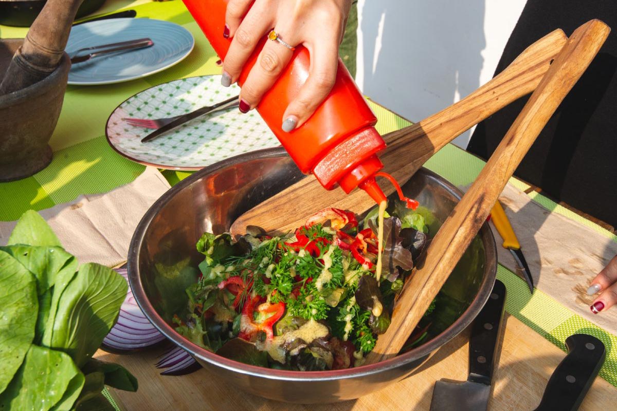 A person is attending a cooking class and squeezing a red sauce into a bowl of salad.