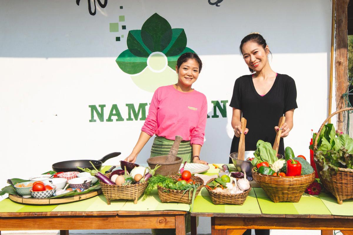 Two women participating in a cooking class, standing in front of a table with baskets of vegetables.