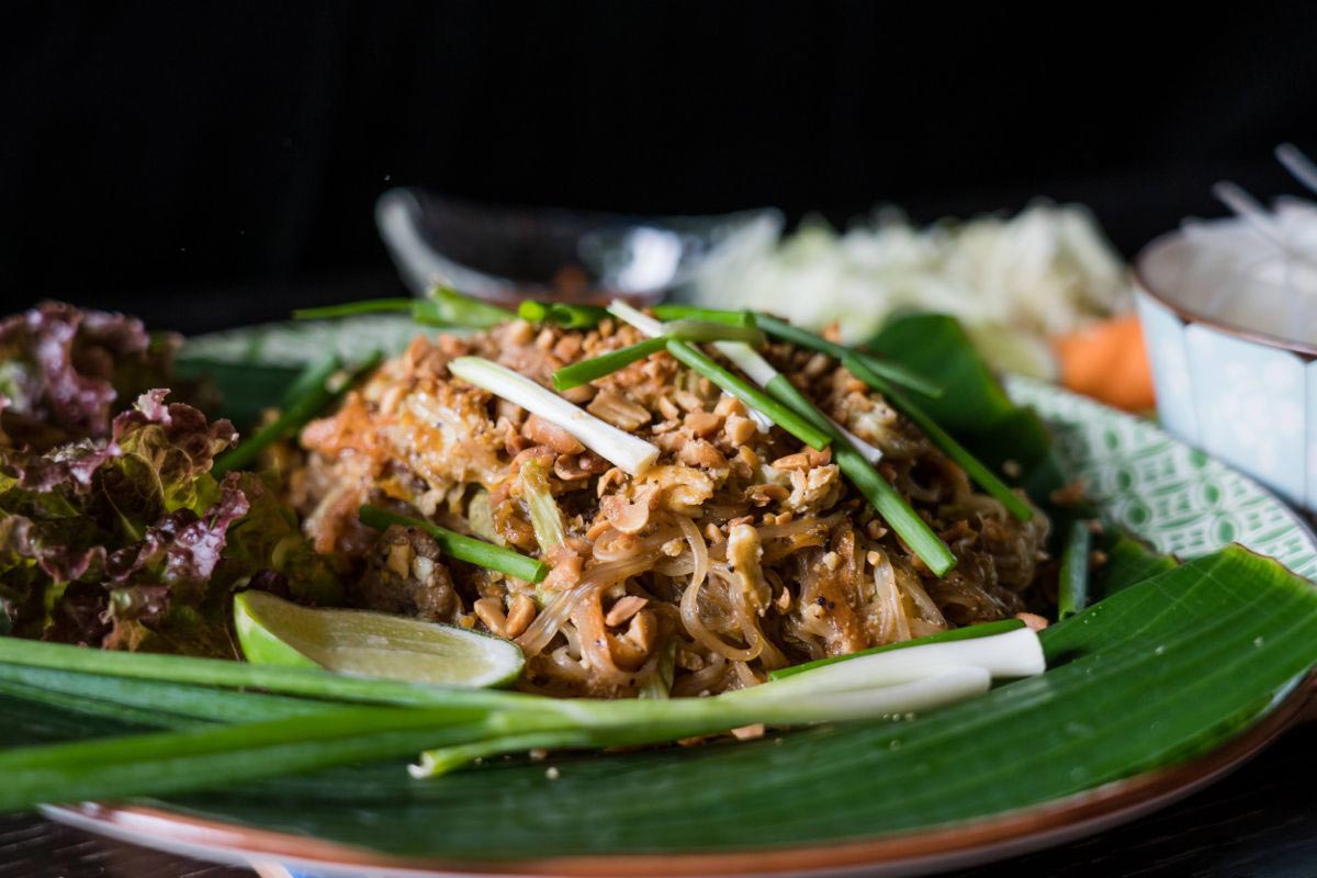 A plate of thai food on a green leaf, resting on a table.