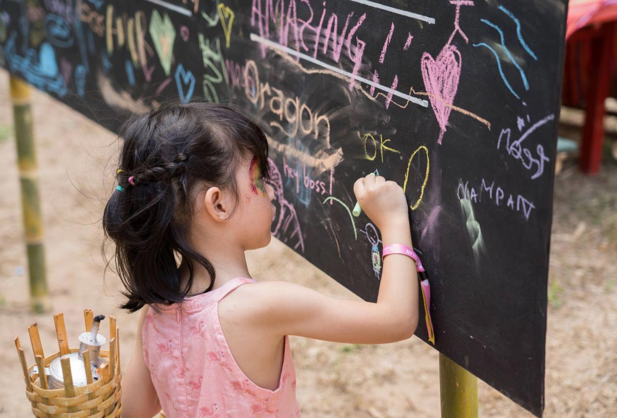 A little girl is drawing on a chalkboard at an outdoor playground.
