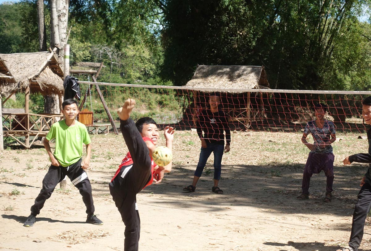 A group of people playing soccer on a dirt field situated in an outdoor playground.