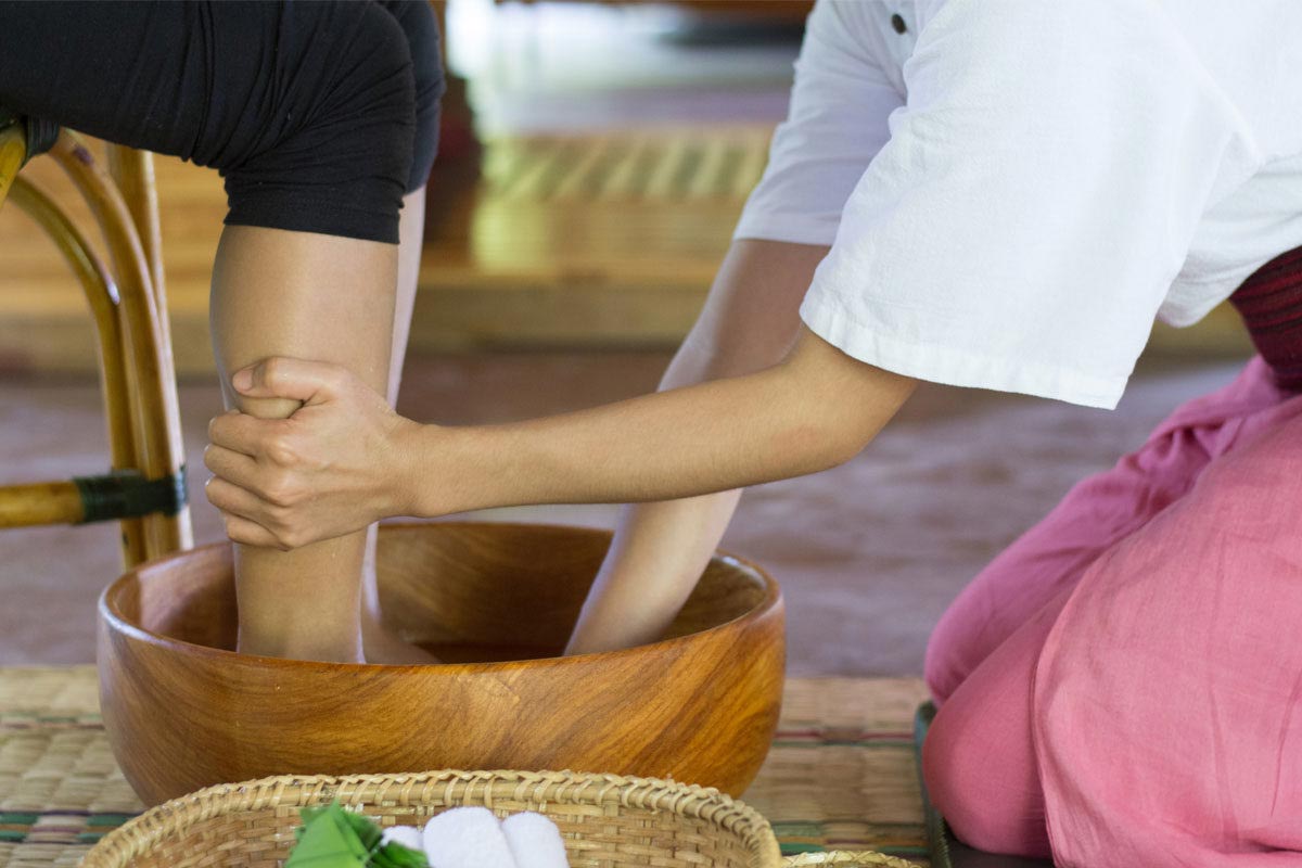 A woman experiencing wellbeing with a foot massage in a wooden bowl.