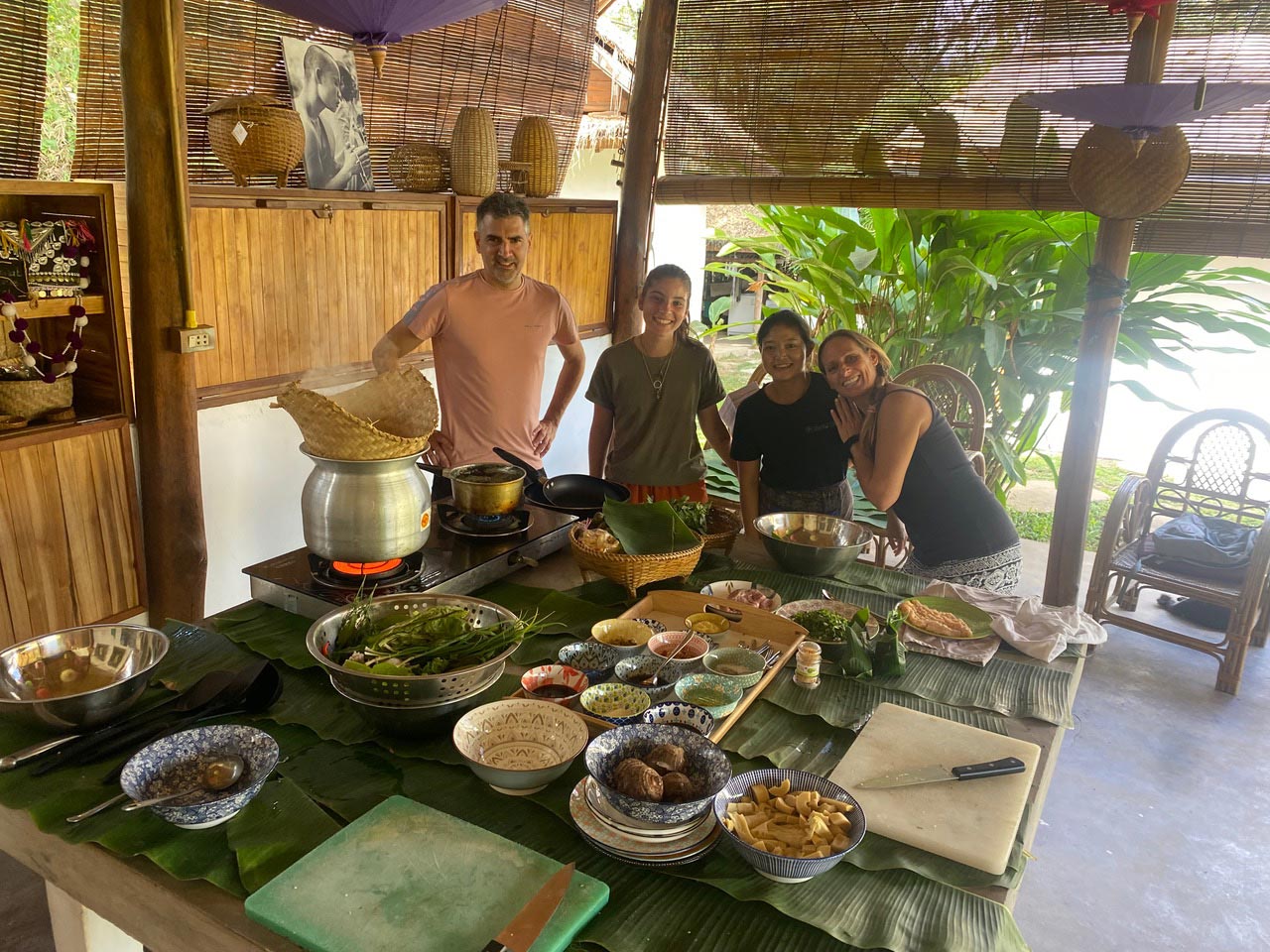 A group of people attending a cooking class, standing around a table with food on it.
