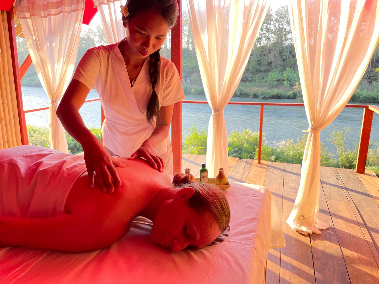 A woman receiving a soothing spa massage on a bed alongside a serene river.