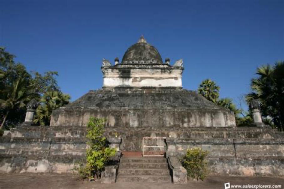 A large stone pagoda in Laos surrounded by a tranquil field.