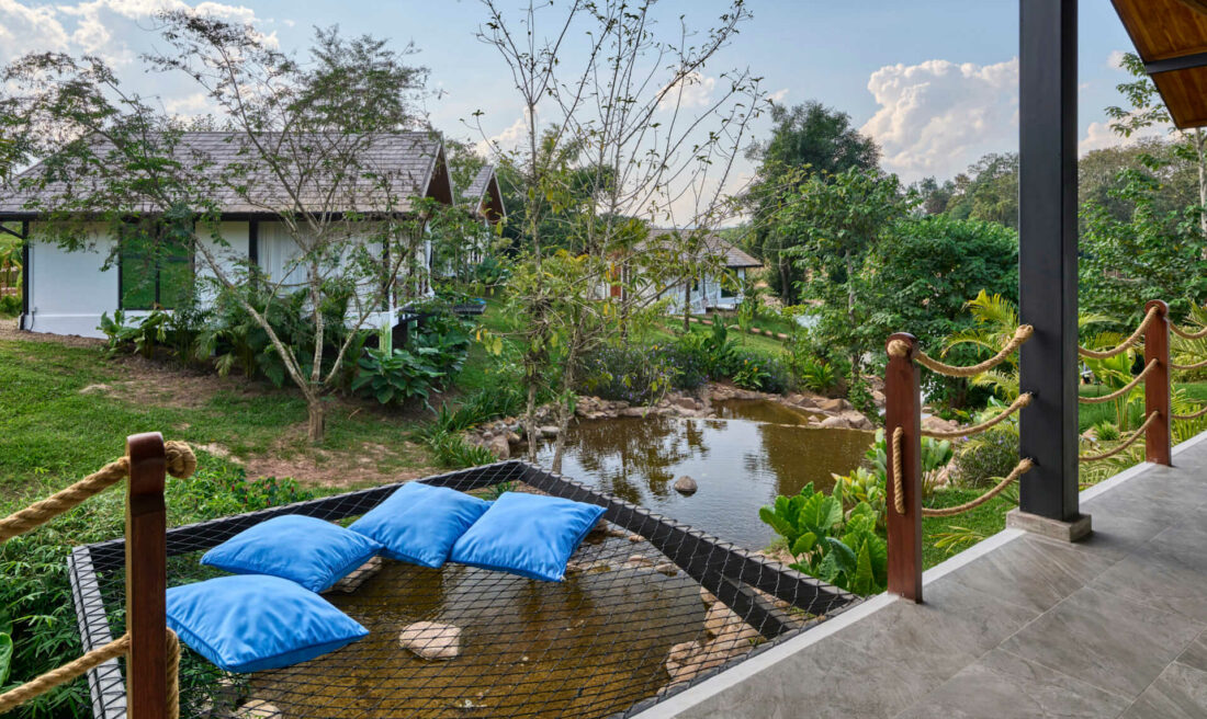 A Luang Prabang inspired balcony overlooking a pond with blue pillows.