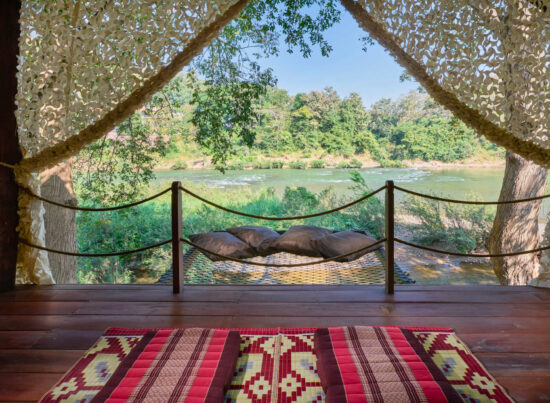 A luang prabang room with a hammock overlooking a river.