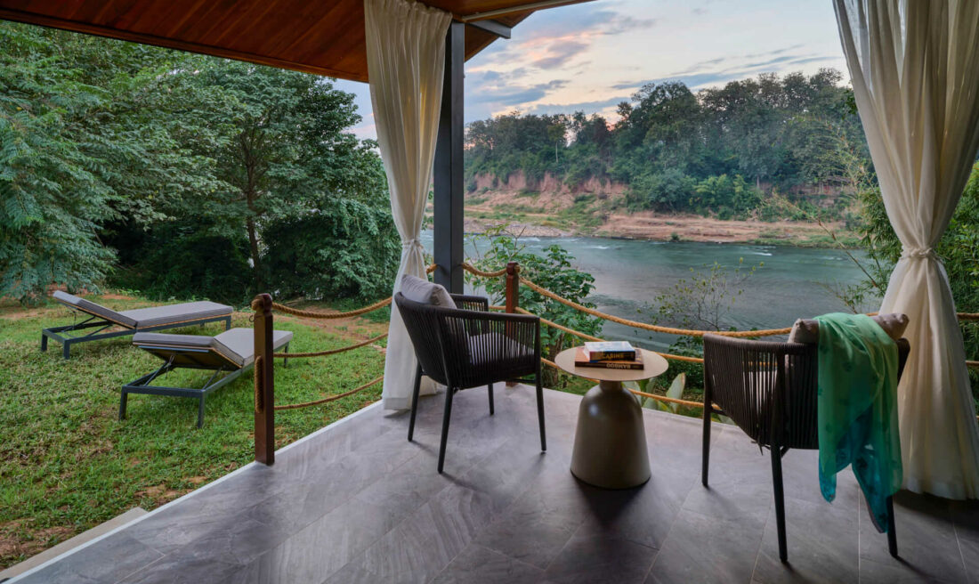 A scenic balcony in Luang Prabang overlooking a river with chairs and a table.