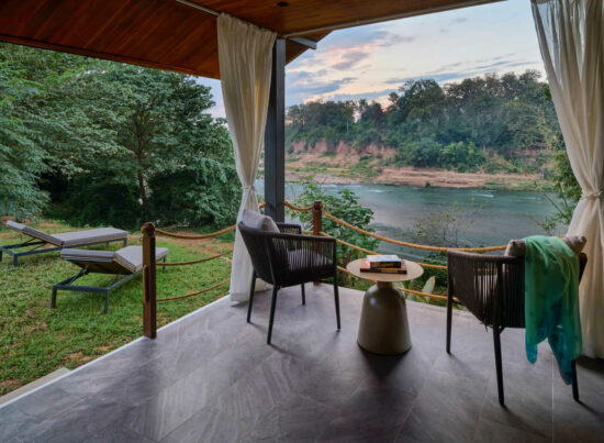A scenic balcony in Luang Prabang overlooking a river with chairs and a table.