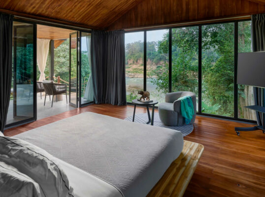 A Luang Prabang bedroom with large windows overlooking a river.