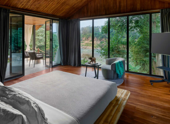 A Luang Prabang bedroom with large windows overlooking a river.