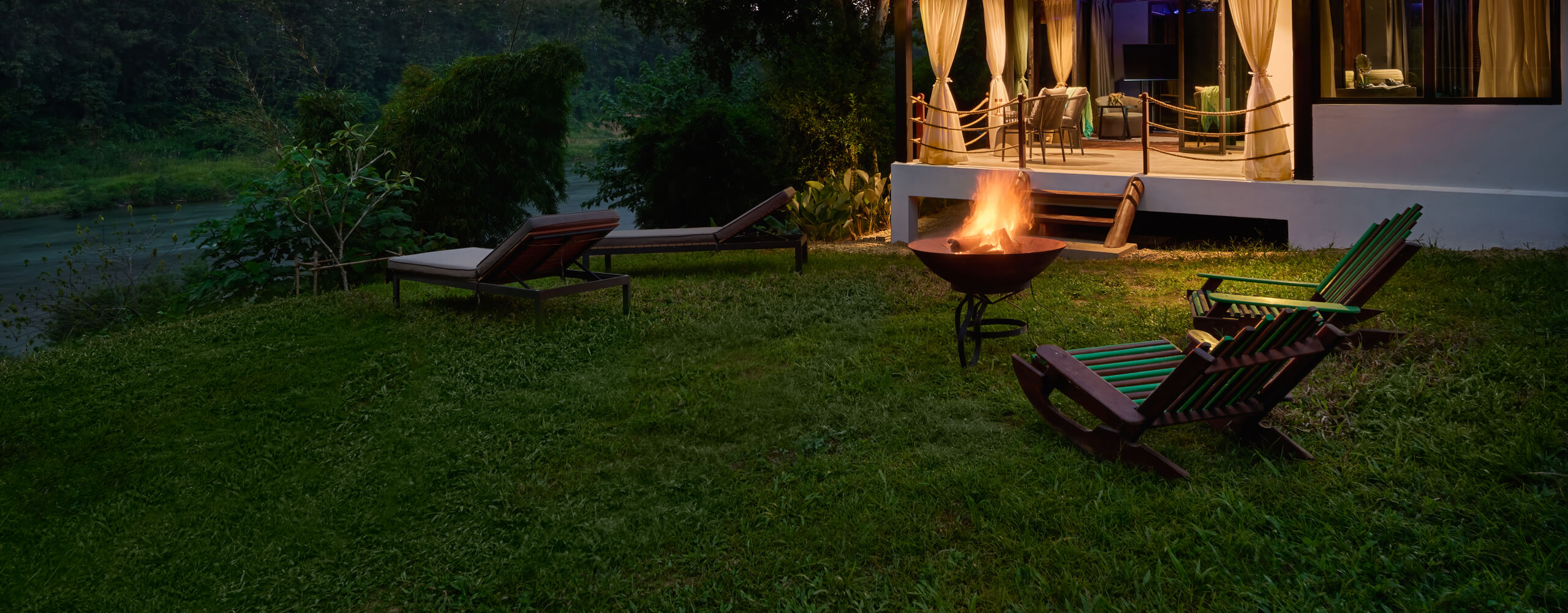 A Luang Prabang house with lawn chairs and a fire pit near a river.