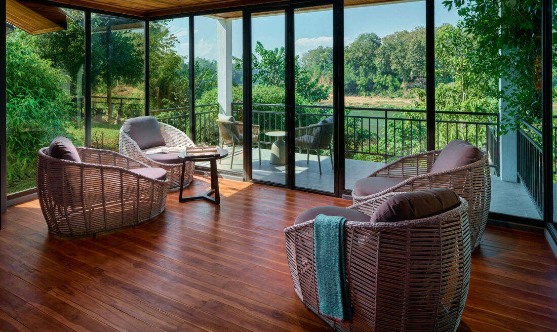 A screened in porch with wicker furniture and a breathtaking view of Luang Prabang.