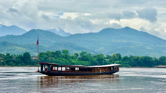 A Luang Prabang boat on a river with mountains in the background.