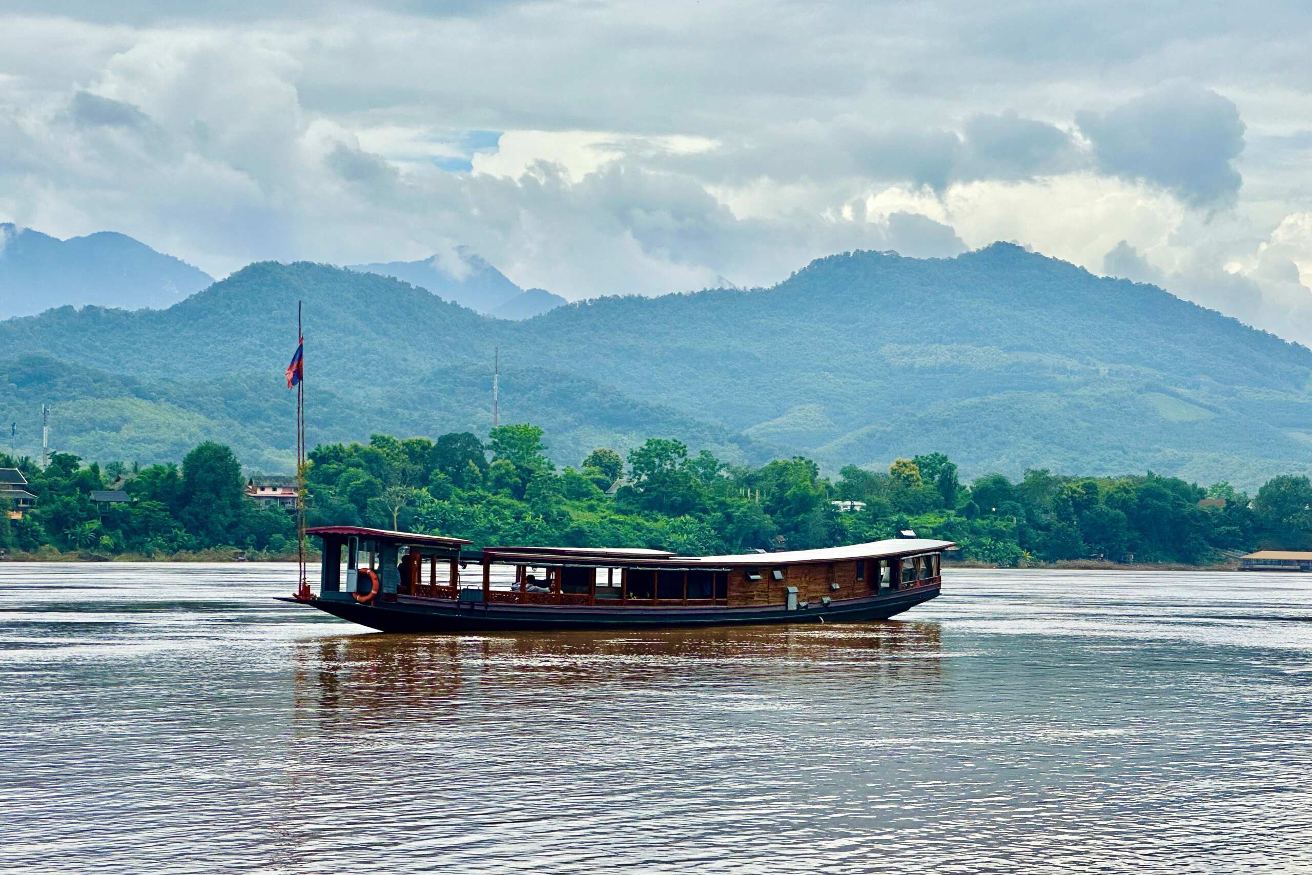 A Luang Prabang riverboat with mountains in the background.