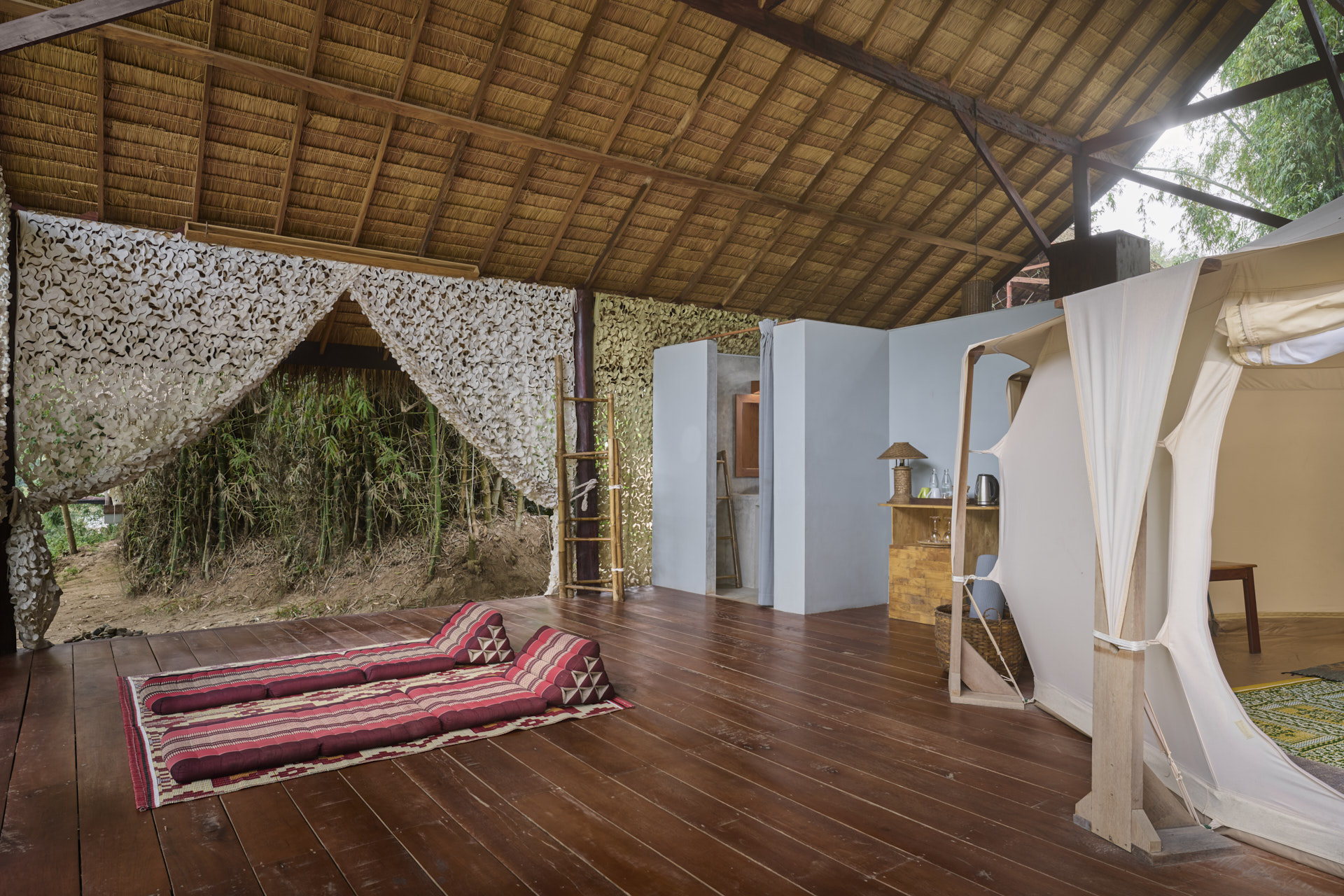 Open-air yoga studio with bamboo roof, wooden floors, red mats, and white drapes in a natural setting near Luang Prabang.